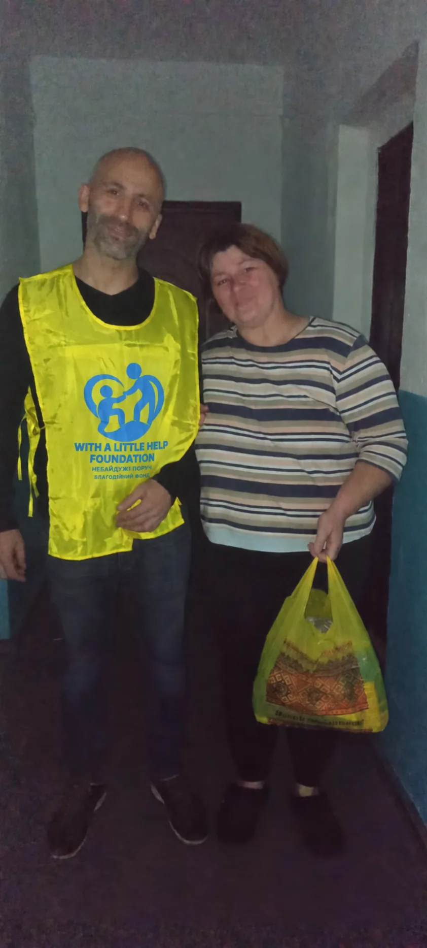 A team member and a woman in a striped top holding a yellow bag in a hallway.