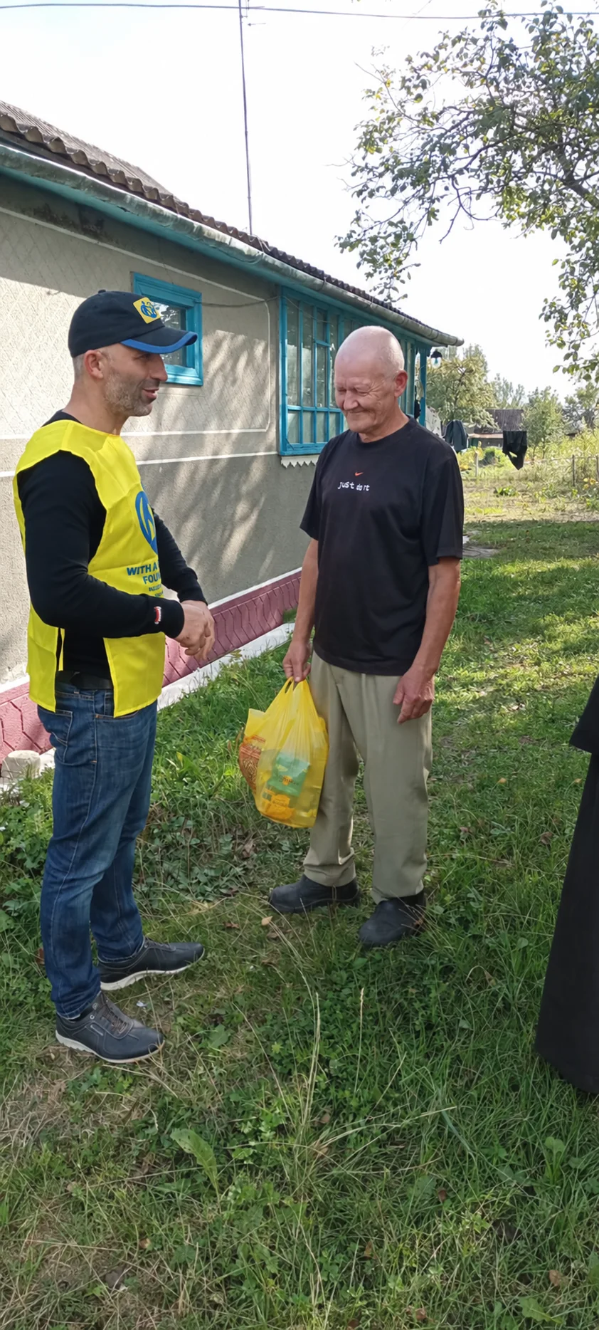 A team member talking with a man holding a yellow bag beside a house.